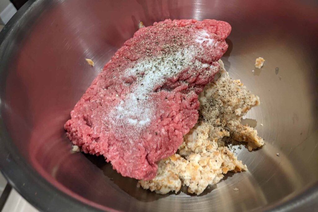 Mixing bowl filled with seasoned raw ground beef and soaked bread