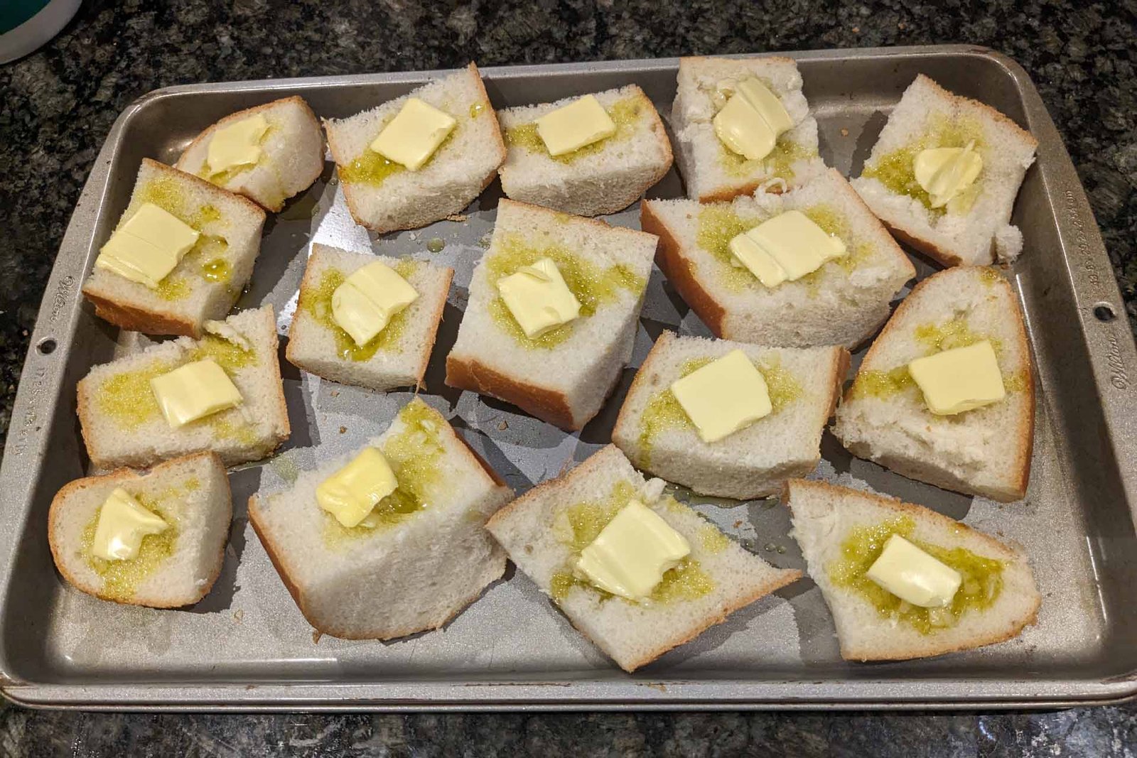 Pieces of bread topped with garlic, olive oil, and butter on a baking sheet