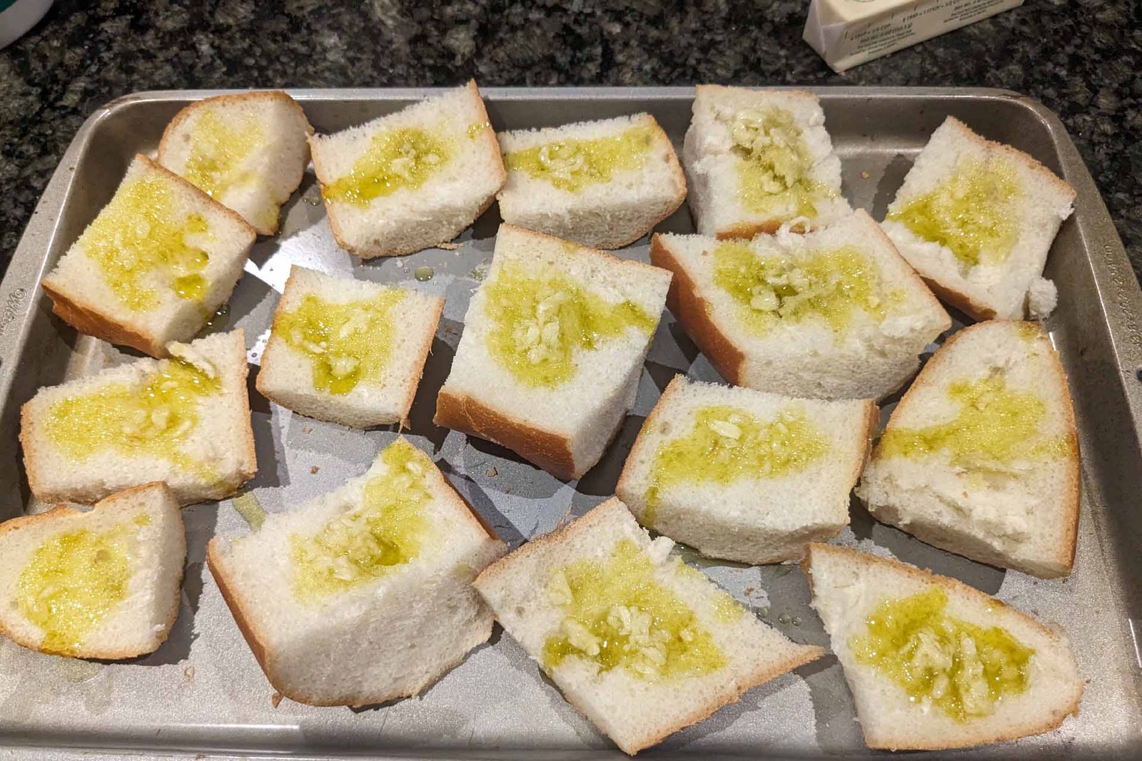 Pieces of bread topped with garlic and olive oil on a baking sheet