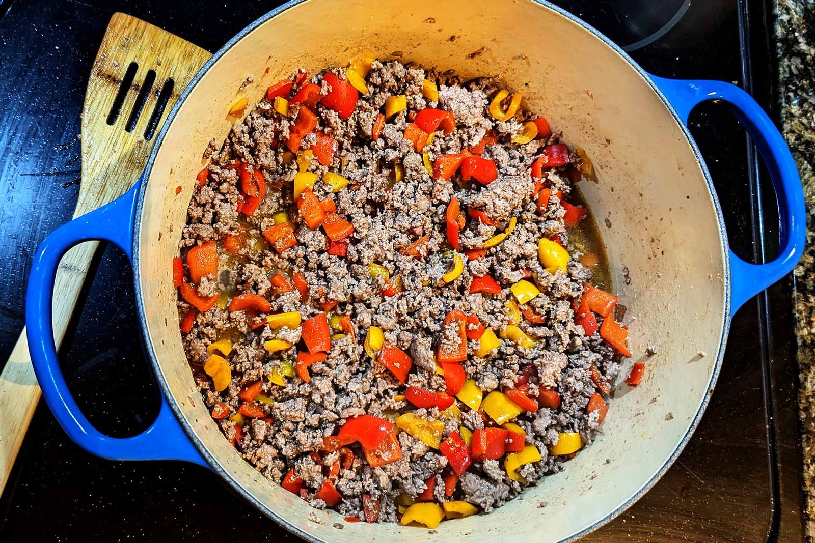 Ground beef and diced red and yellow sweet peppers in a pot on the stove