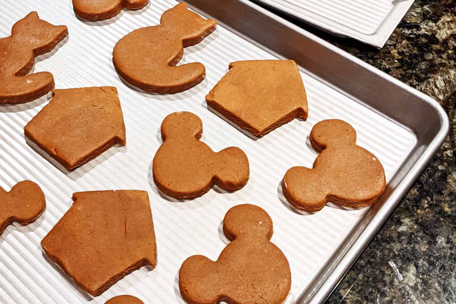 Gingerbread dough cut into various shapes, laid out on a baking sheet