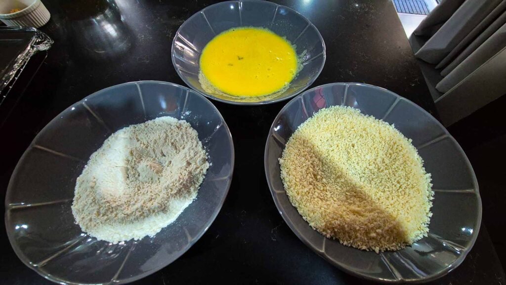 Bowls of raw scrambled egg, panko breadcrumbs, and flour