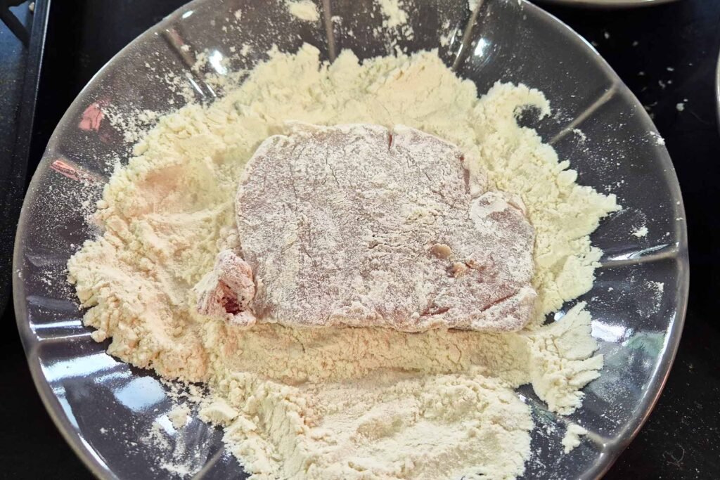 Raw pork cutlet laying in a bowl of flour